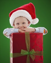 Caucasian boy in Santa hat leaning on Christmas gift