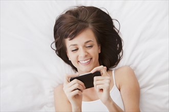 Caucasian woman laying in bed text messaging on cell phone
