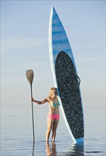 Caucasian woman standing in water with paddle board