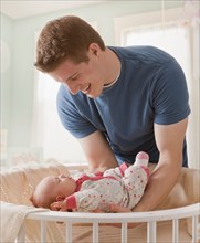 Caucasian father lifting baby girl from crib