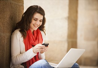 Caucasian woman sitting with laptop and text messaging on  cell phone