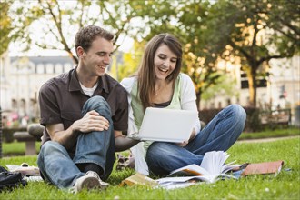 Caucasian students sitting in grass looking at laptop