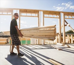 Caucasian man carrying lumber on construction site