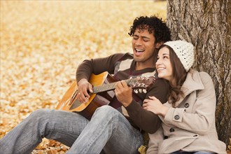 Man playing guitar for girlfriend in autumn leaves
