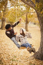 Couple playing on swing in autumn leaves