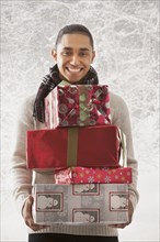 Hispanic man holding stack of presents in snow