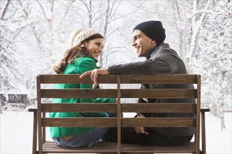 Couple sitting on park bench in snow