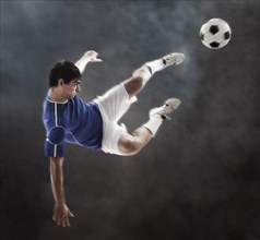 Hispanic soccer player kicking ball in mid air