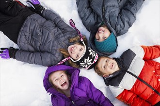 Caucasian children laying in snow outdoors