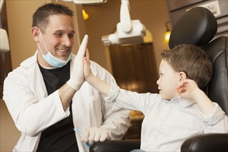 Caucasian dentist and boy high fiving in office