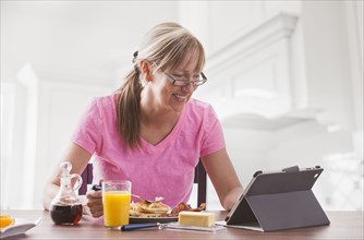 Caucasian woman using tablet computer at breakfast