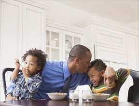Father kissing sons at breakfast table