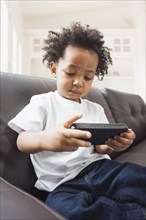 Mixed race boy playing with cell phone on sofa