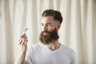 Bearded Caucasian man examining razor