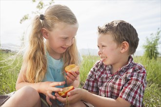 Caucasian children sharing fruit outdoors