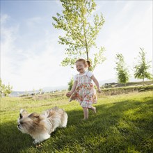 Caucasian girl chasing dog in grass
