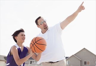 Father teaching son to play basketball in driveway