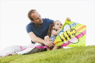 Caucasian father and daughter fixing kite in grass