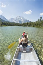 Caucasian mother and daughter paddling canoe on lake