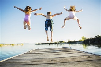 Caucasian children jumping off dock into lake