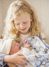 Caucasian girl holding newborn baby brother