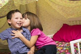 Caucasian children kissing in blanket fort