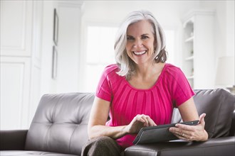 Portrait of smiling Caucasian woman using digital tablet on sofa