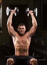 Caucasian man with bare chest lifting dumbbells overhead