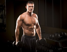 Confident Caucasian man holding dumbbells in gym