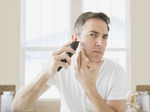 Caucasian man shaving in bathroom