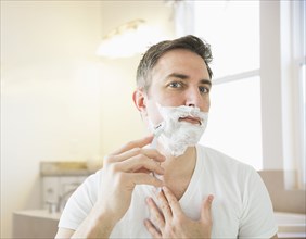 Caucasian man shaving in bathroom