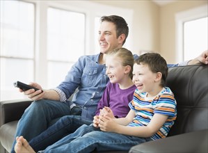 Caucasian father and children watching television on sofa