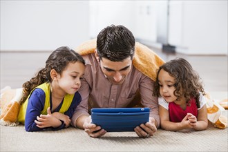 Father and daughters using tablet computer on living room floor