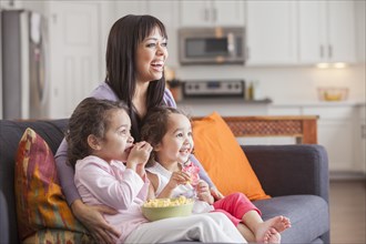 Mother and daughters watching television on sofa