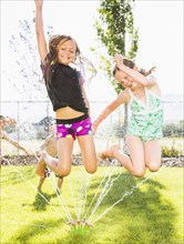 Caucasian girls playing in sprinkler in backyard