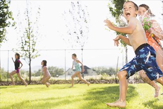 Caucasian children playing in sprinkler in backyard