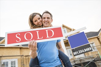 Caucasian couple holding sold sign near house under construction