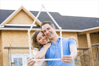 Caucasian couple holding frame near house under construction