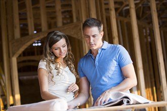 Caucasian couple reading blueprints in house under construction