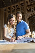Caucasian couple marking blueprints in house under construction