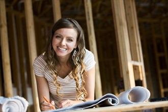 Caucasian woman marking blueprints in house under construction