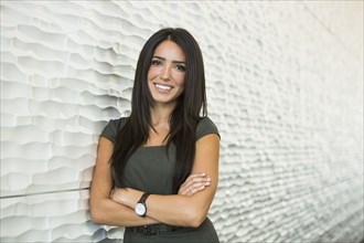 Hispanic businesswoman smiling near wall