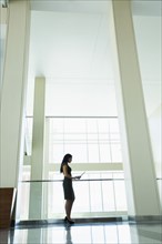 Hispanic businesswoman using digital tablet in office hallway