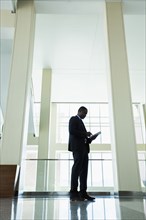 Black businessman using digital tablet in office hallway
