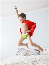 Caucasian boy playing superhero on bed