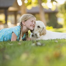 Caucasian girl nuzzling pet dog on grassy lawn
