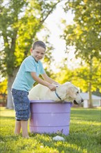Caucasian boy washing pet dog in backyard