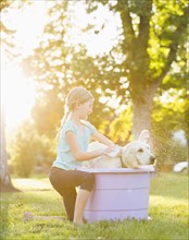 Caucasian girl washing pet dog in backyard
