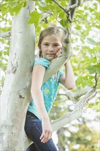 Smiling Caucasian girl climbing tree outdoors