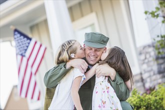 Returning Caucasian soldier hugging daughters